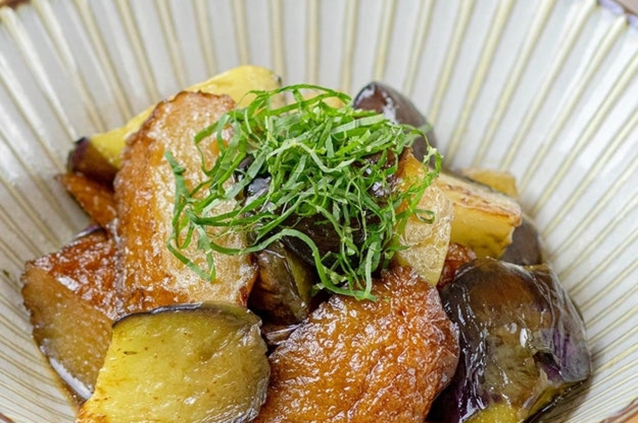 揚げたナスと魚の天ぷらが盛られた和風の皿に、細かく刻んだ野菜がトッピングされています。