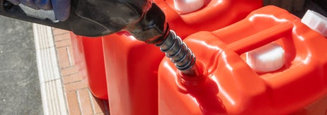 赤いプラスチック容器にノズルを使って液体を注ぐ手。