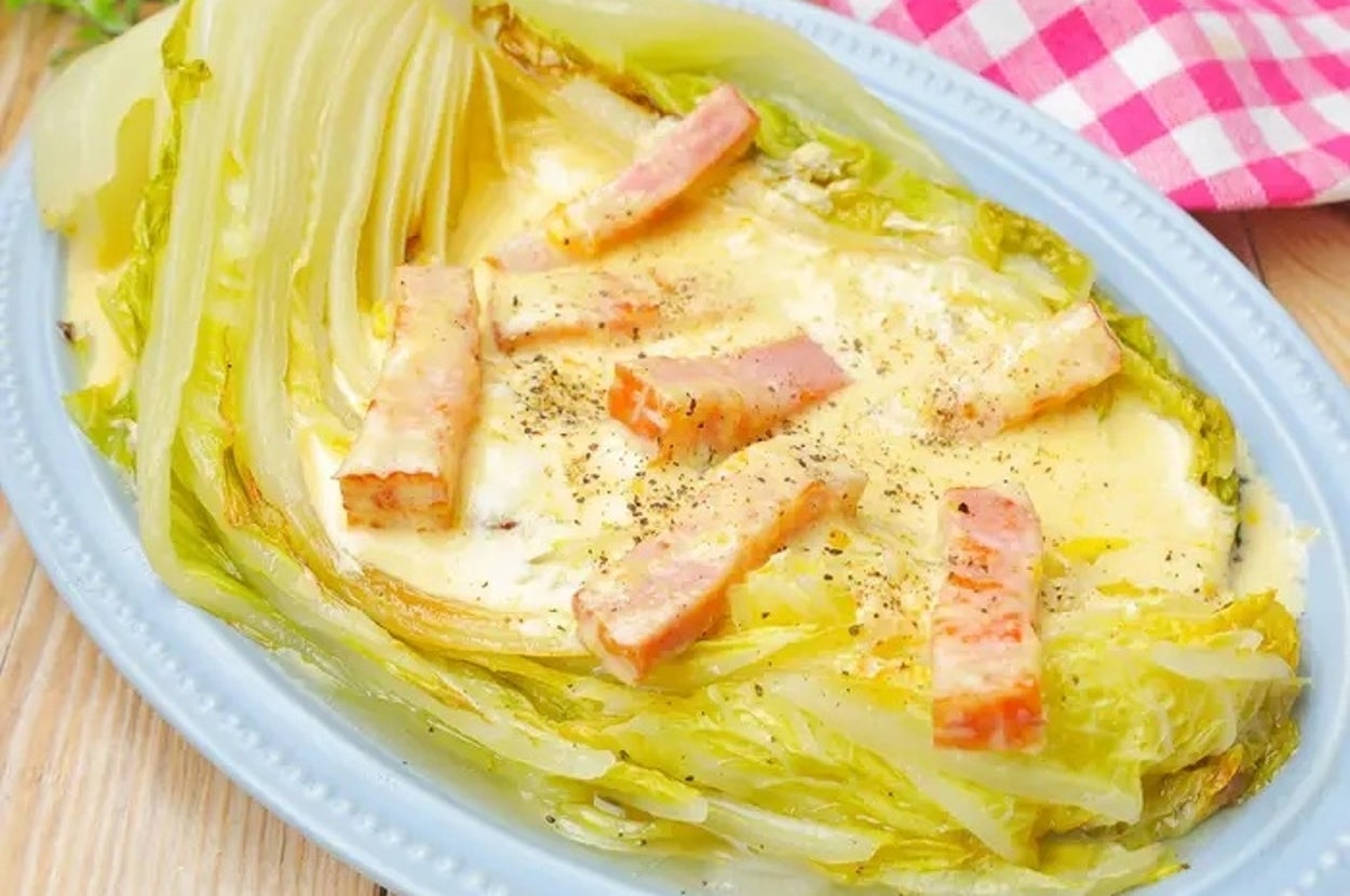 キャベツとベーコンの具材が載ったグラタン。皿の横にチェック柄の布が見える。