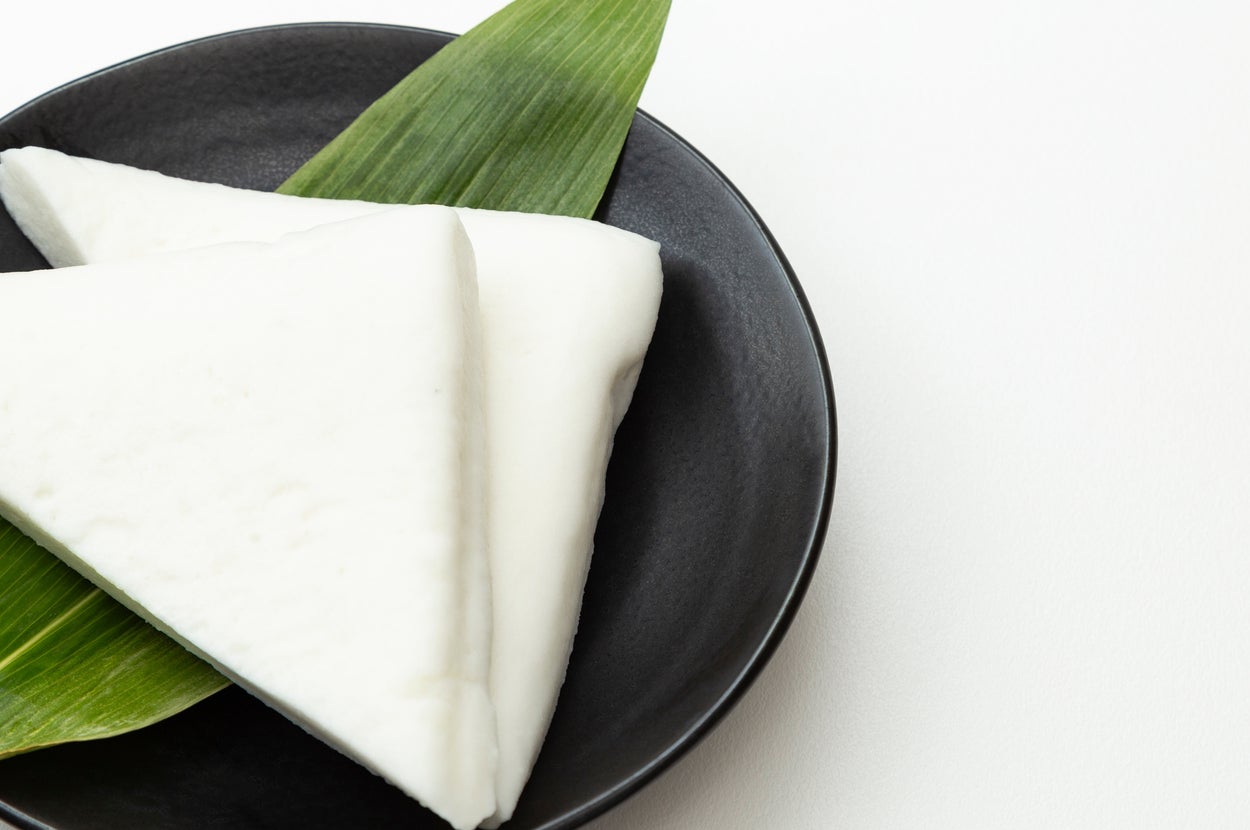 三角形の白い和菓子が葉の上に盛り付けられた黒い皿にのっています。