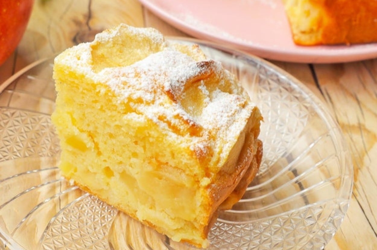 皿に盛られた焼きたてのアップルケーキの一切れ。背景にケーキ全体が見える。