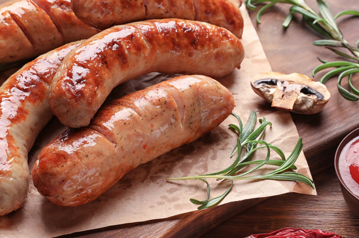 木製の板に盛られた焼きソーセージ4本とローズマリーの装飾、ケチャップの小皿が添えられています。