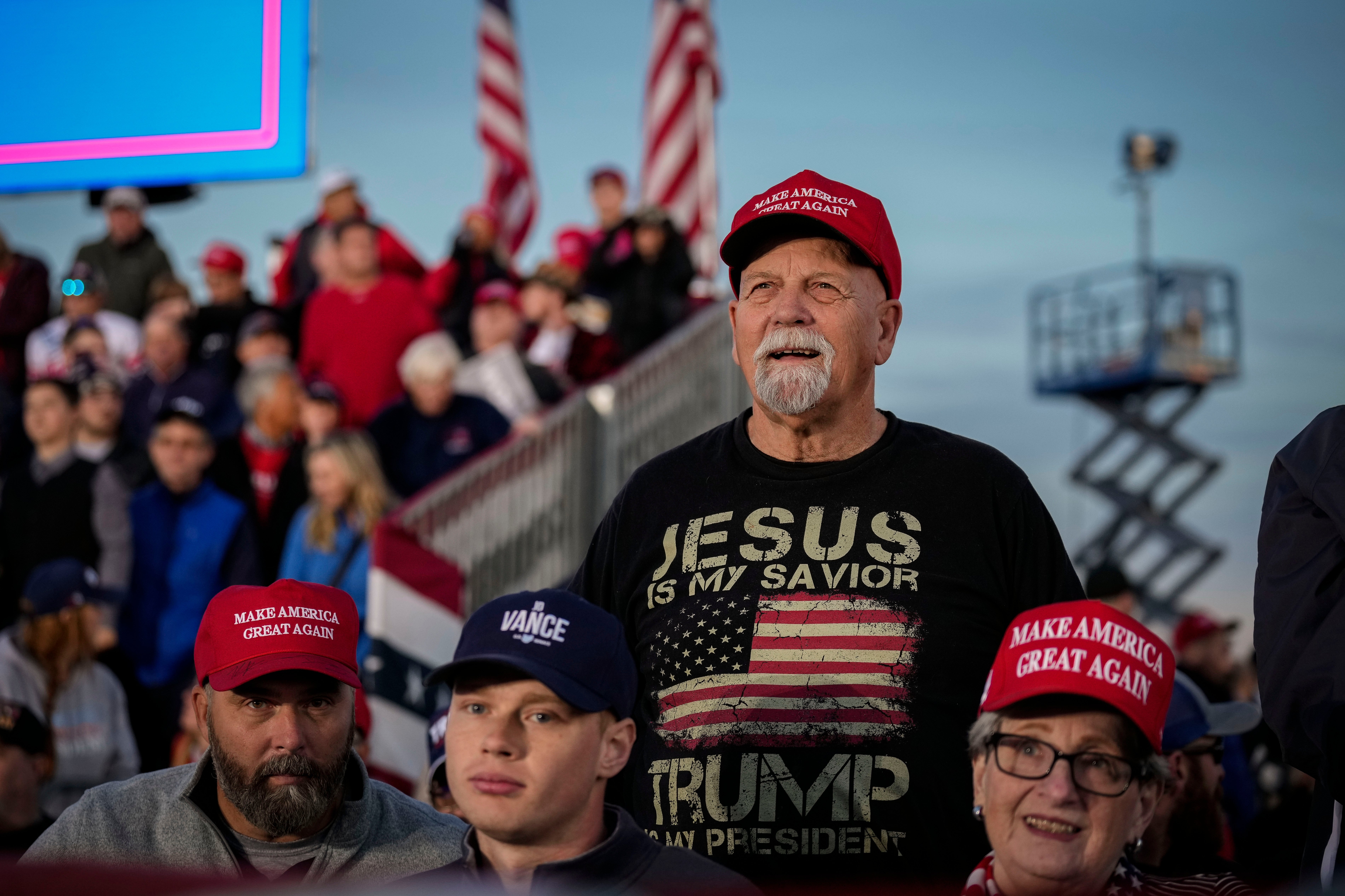 Group of radical   astatine  a rally; 1  antheral   stands retired  with a "Jesus is My Savior, Trump My President" garment  and a "Make America Great Again" cap