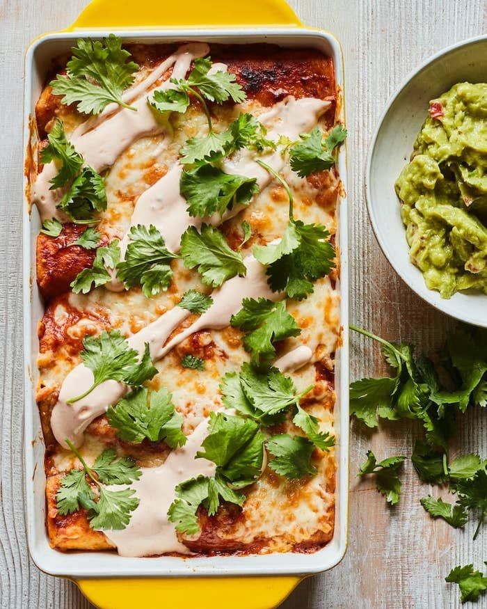 Baked enchiladas topped with cilantro and sauce in a dish next to a bowl of guacamole on a wooden table
