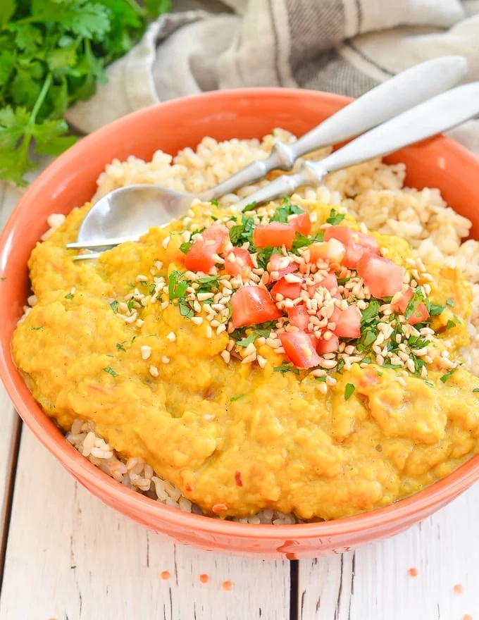 A bowl of rice topped with a creamy lentil curry, diced tomatoes, and sesame seeds, with a spoon and fork resting on the side