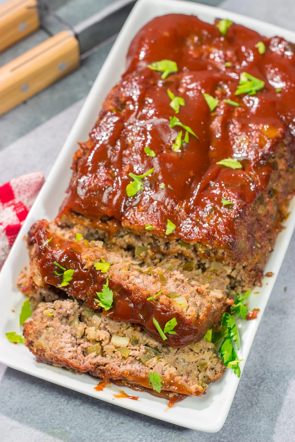Sliced meatloaf on a white platter, topped with a glaze and garnished with herbs