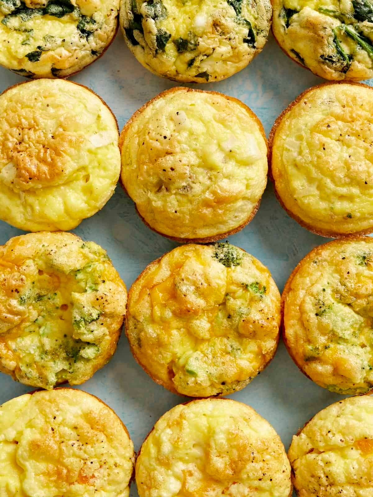 A dozen freshly baked egg muffins with spinach and cheese on a light surface