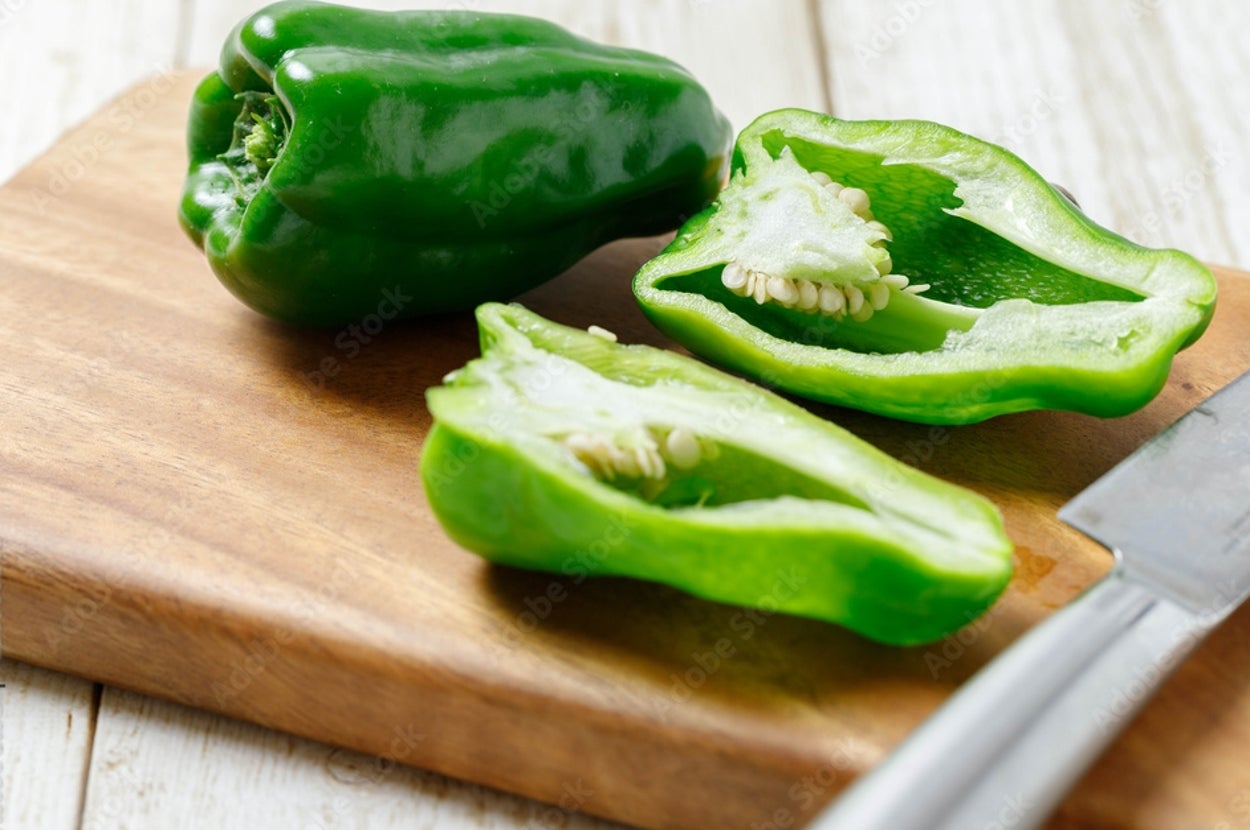 カットされて種が見えるピーマンが木のまな板に置かれ、横にナイフがある。