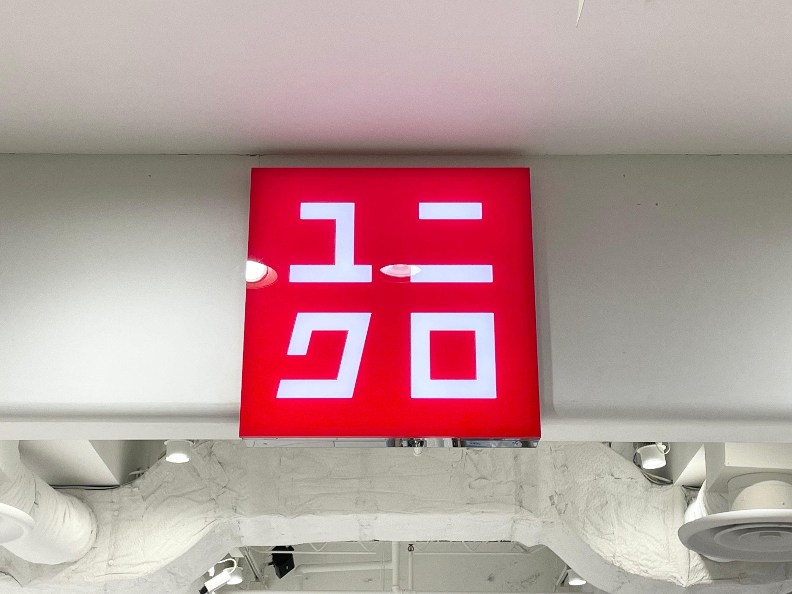 A red Uniqlo store sign with stylized characters, mounted on a white wall