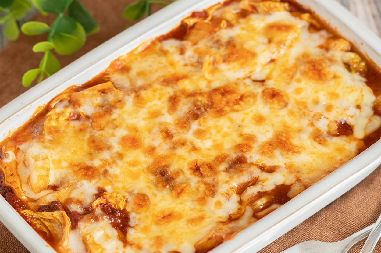 陶器の皿に盛られた焼きたてのラザニア。脇にカトラリーと植物がある。