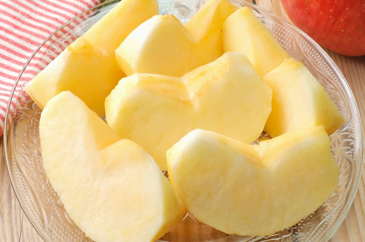 ガラスの皿に並んだりんごのスライス。背景に赤と白のストライプ布とりんごも見える。