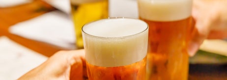 複数の手がビールジョッキを持って乾杯している様子。テーブルにメニューが見える。