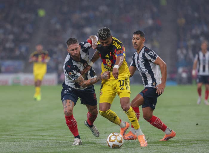 Soccer players in intense play, two defending one in yellow jersey controlling the ball. Stadium audience blurred in background