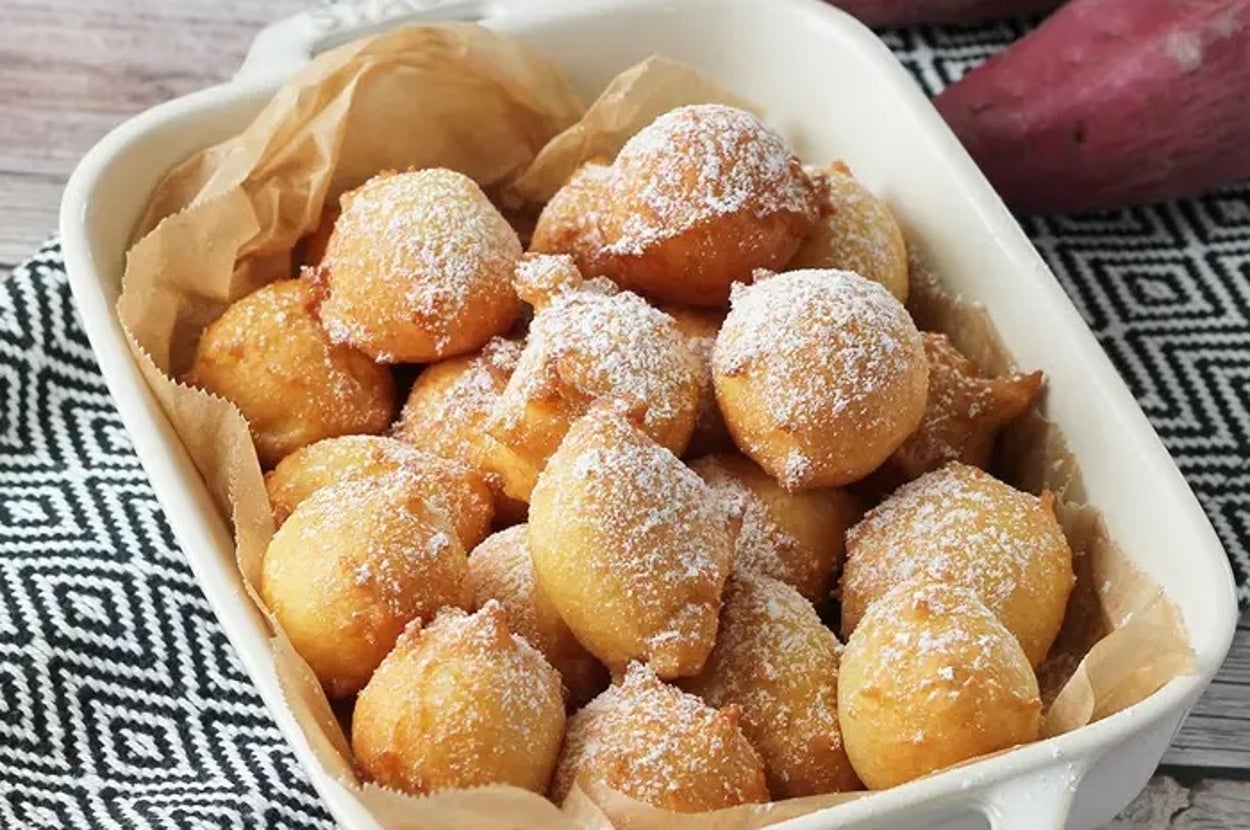 白い皿に盛られたさつまいもドーナツが砂糖をまぶされ、ランチョンマットの上に置かれています。