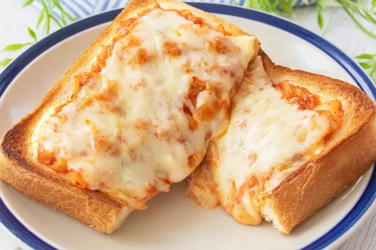 パンの上に溶けたチーズとキムチがのったトーストが皿に盛られている。背景には緑の植物が見える。