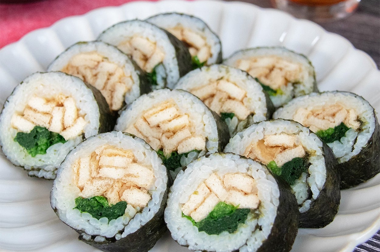 お皿に盛られた油揚げとほうれん草ののり巻き。中には油揚げとほうれん草が巻かれている。背景に飲み物がある。