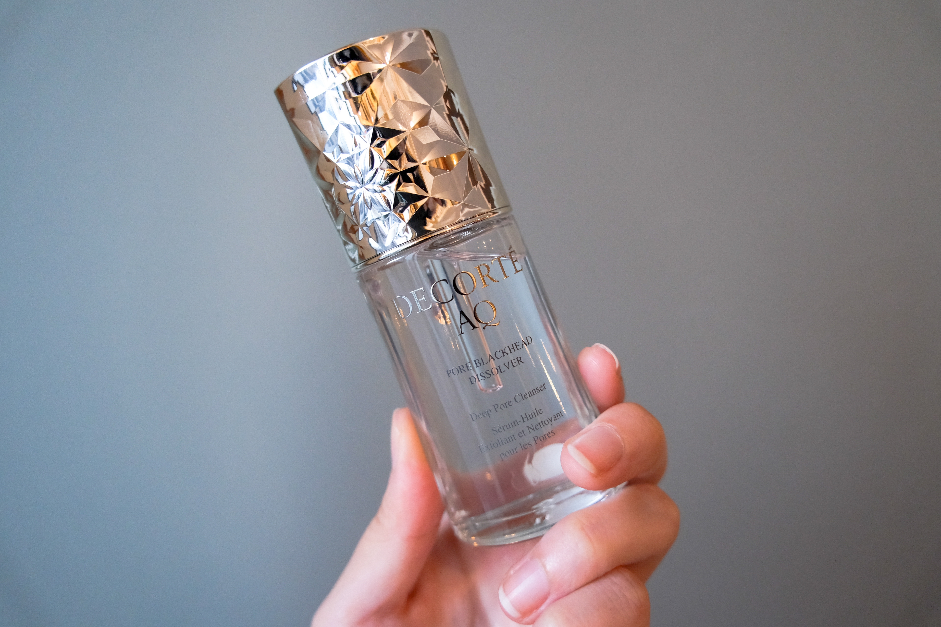 手に持たれた高級スキンケア製品のボトル。銀色のキャップが特徴的です。