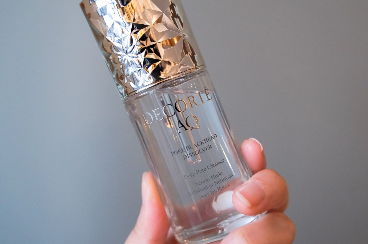 手に持たれた高級スキンケア製品のボトル。銀色のキャップが特徴的です。