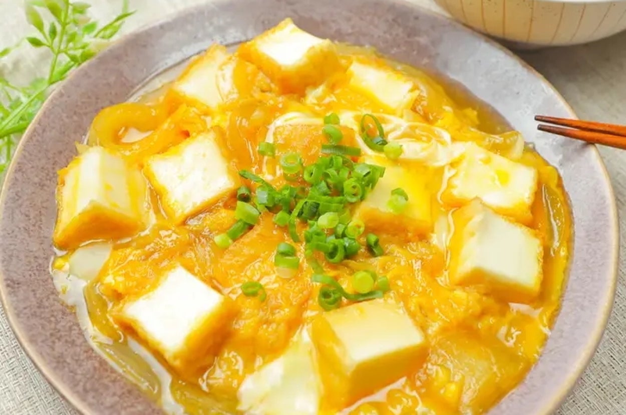 厚揚げと卵の料理が皿に盛られ、ねぎがトッピング。食卓にはご飯と箸が添えられている。