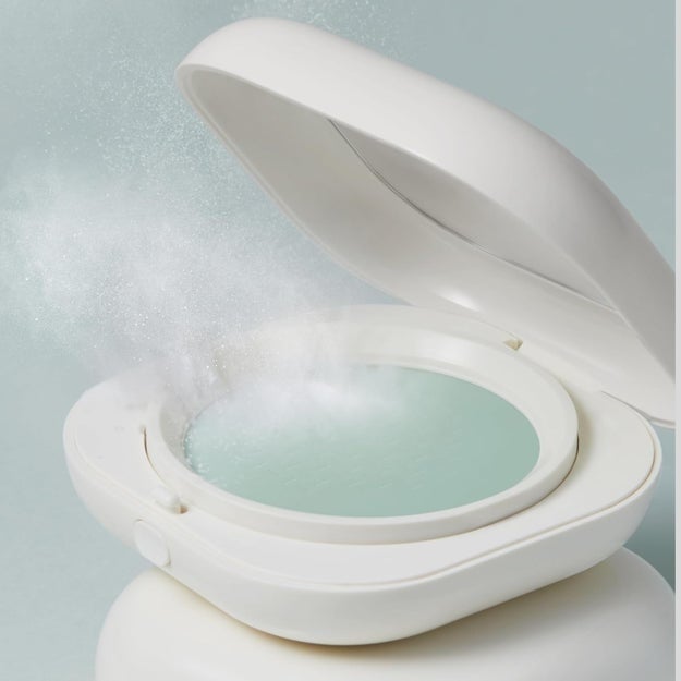 Compact lawsuit  releasing a puff of pulverization  from its lid, suggesting an innovative plan  cleanable   for on-the-go touch-ups