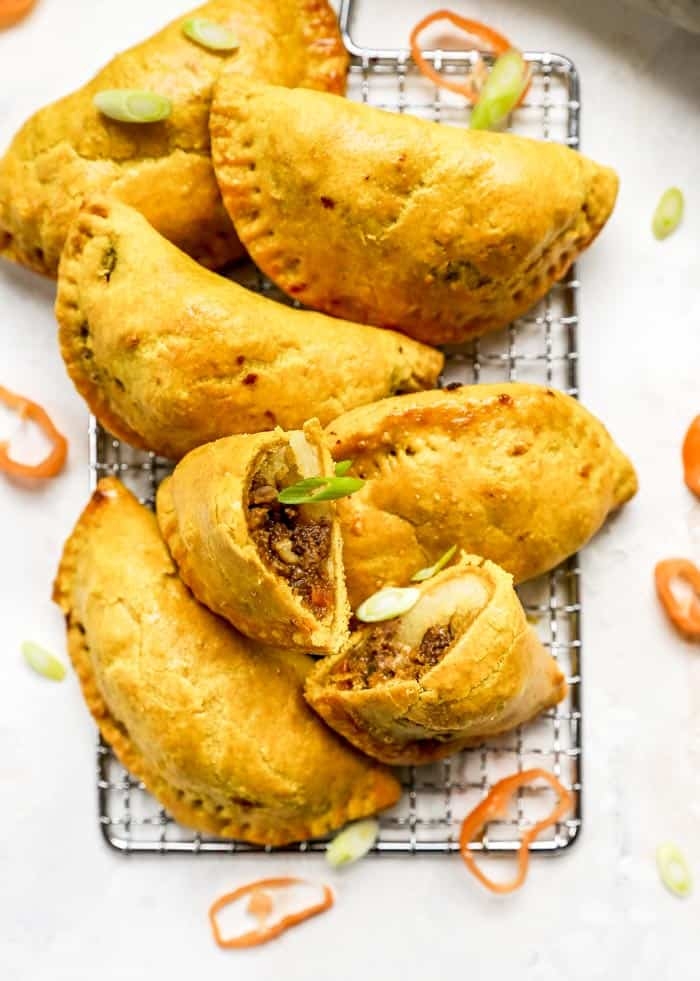 Savory pastries filled with seasoned meat, arranged on a cooling rack, garnished with sliced green onions and peppers