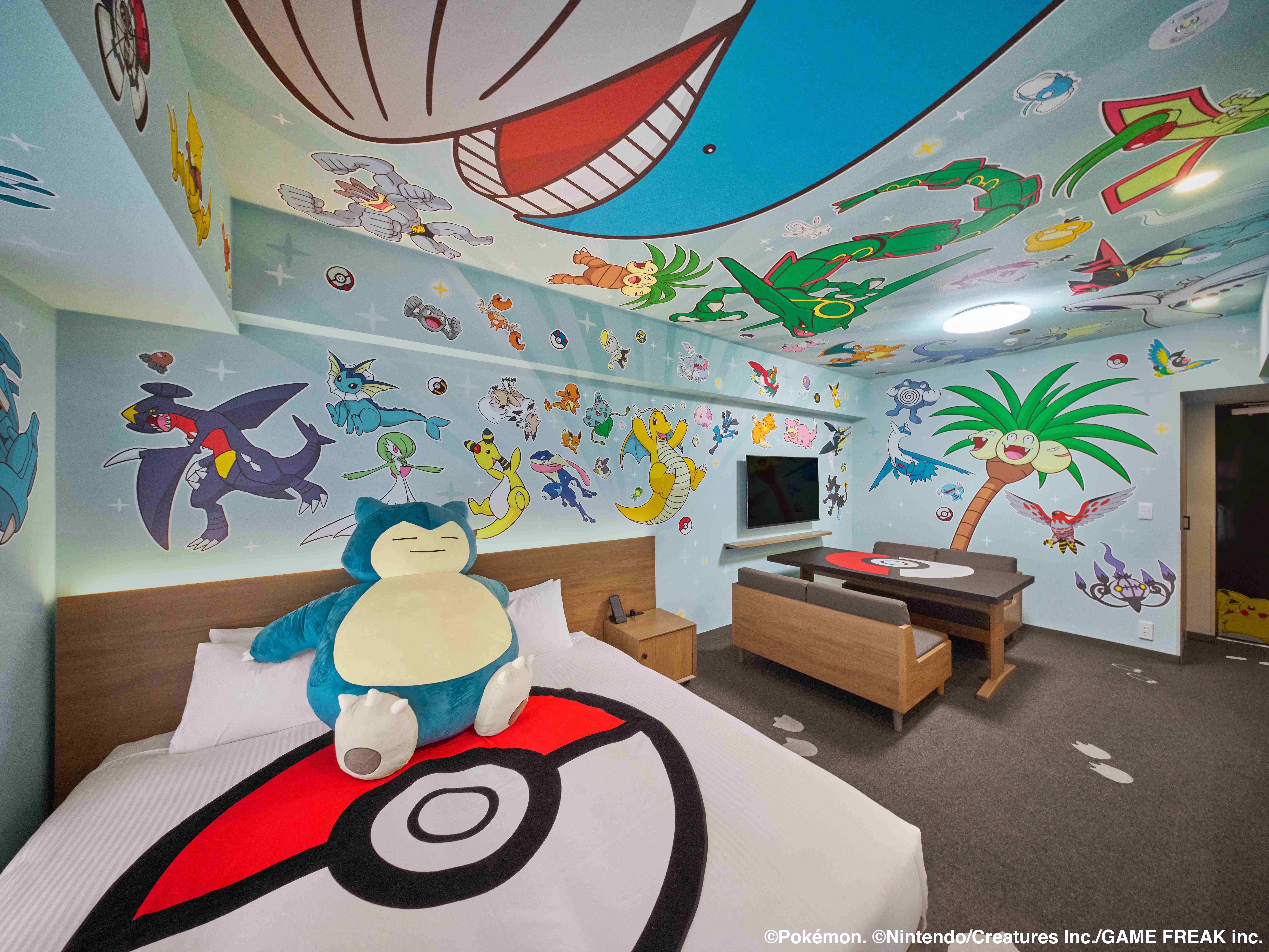 Room decorated with Pokémon-themed murals featuring various characters on the walls and ceiling, with a large Snorlax plush toy on the bed