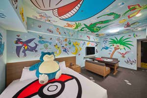 Room decorated with Pokémon-themed murals featuring various characters on the walls and ceiling, with a large Snorlax plush toy on the bed