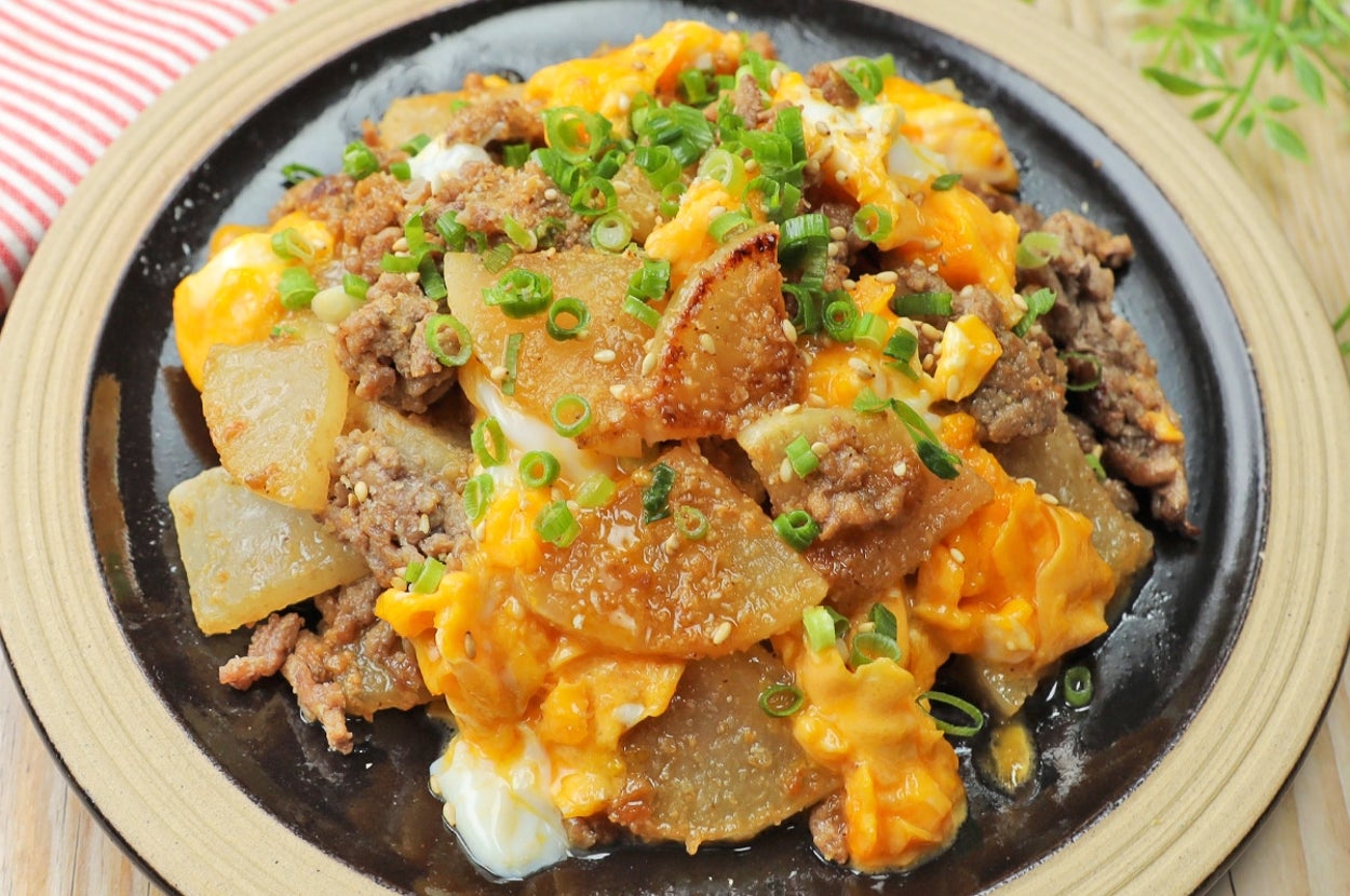 肉と野菜が載った黒いお皿に盛り付けられた卵の料理。緑のねぎがトッピングされています。