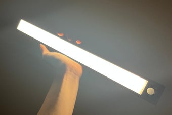 手が明るい直線型のライトを持ち上げているシーン。