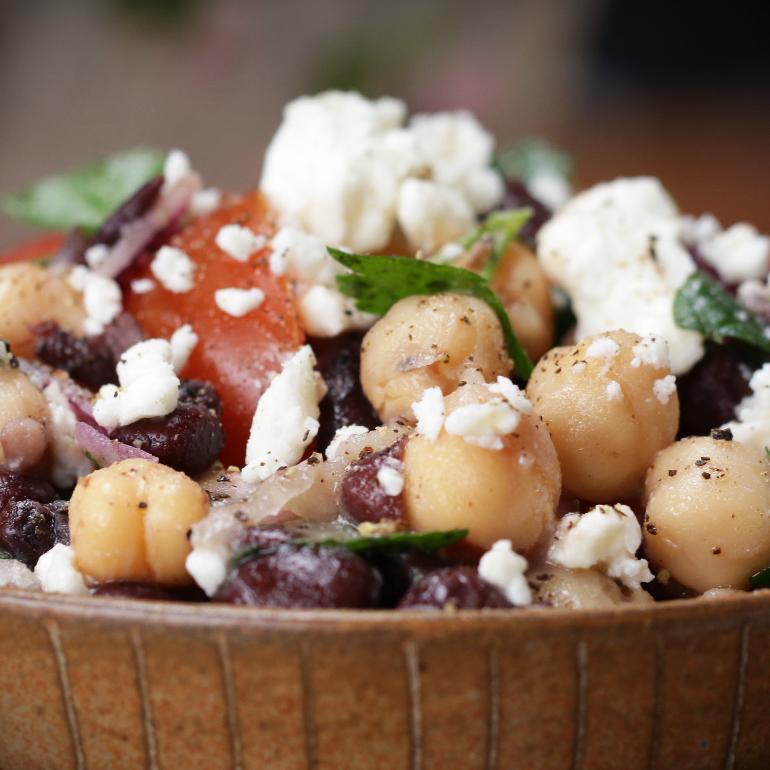 Chickpea salad with tomatoes, feta cheese, black beans, and mint in a wooden bowl