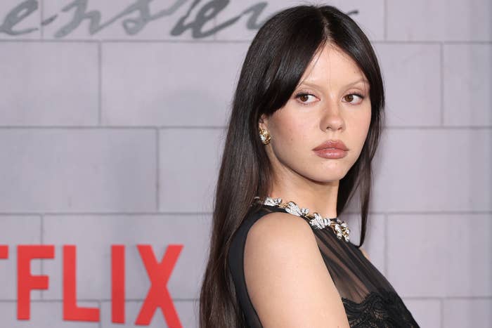 Mia Goth connected  a reddish  carpet successful  elegant formal  with floral necklace, posing against a backdrop with substance   and Netflix logo
