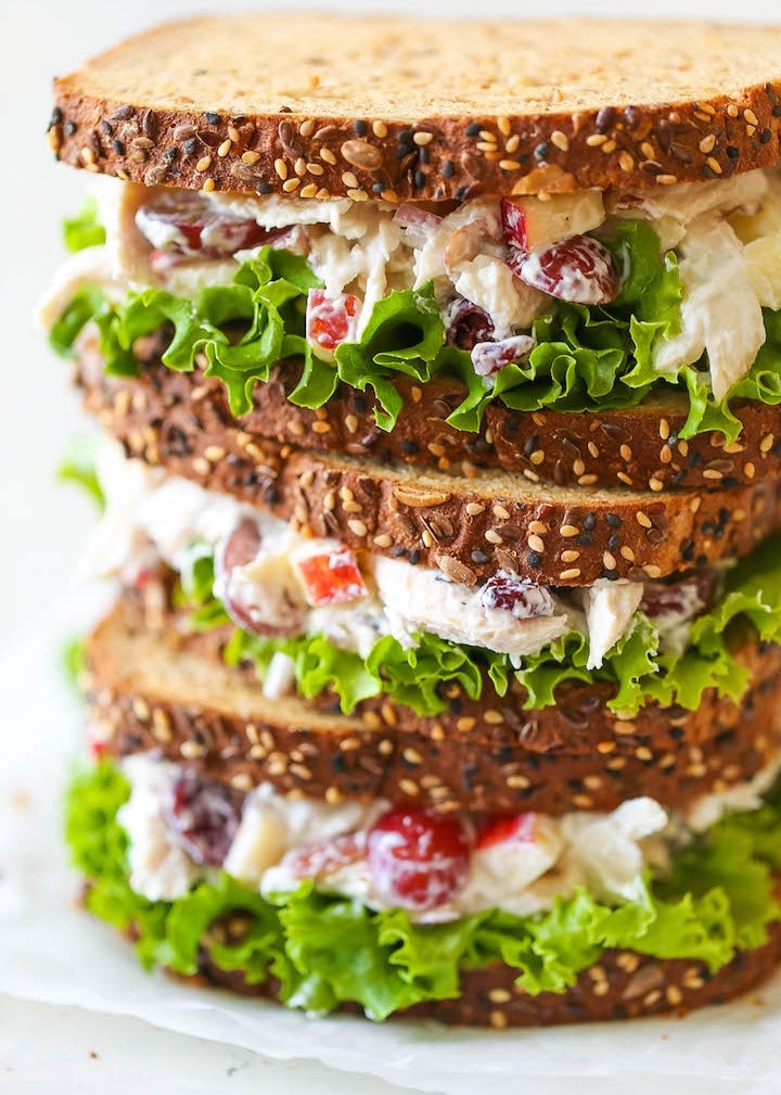 Stacked chicken salad sandwiches with lettuce, apple slices, and tomatoes on seeded bread