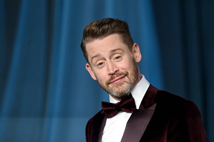 Macaulay Culkin connected  the reddish  carpet wears a velvet tuxedo overgarment   with a bow tie, posing with a flimsy  smile