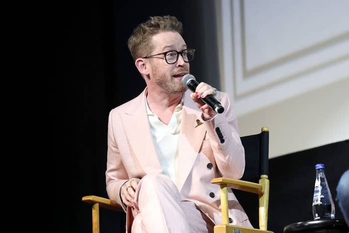 Macaulay Culkin successful  a stylish suit   sits connected  a panel, speaking into a microphone