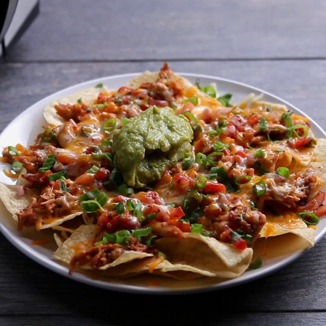 A plate of nachos topped with melted cheese, diced tomatoes, green onions, and a dollop of guacamole in the center