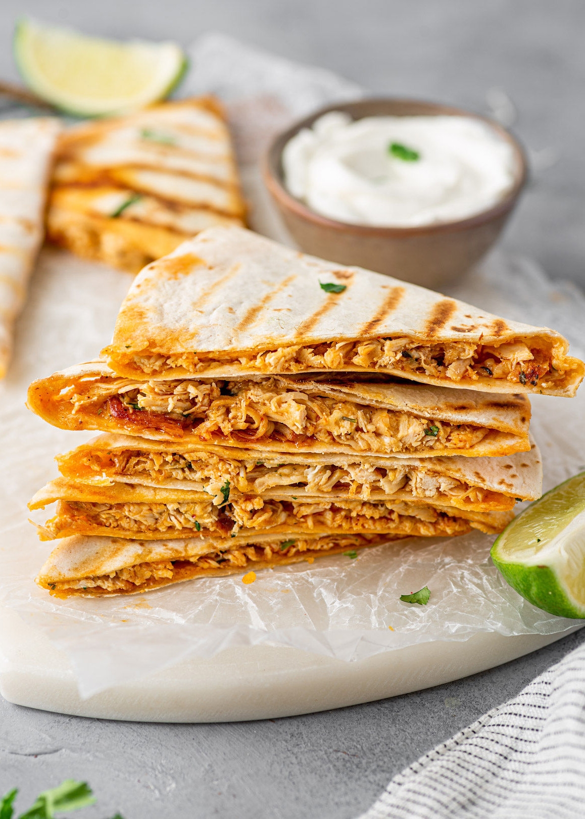 Grilled chicken quesadillas stacked with creamy filling, garnished with lime and a side of sour cream