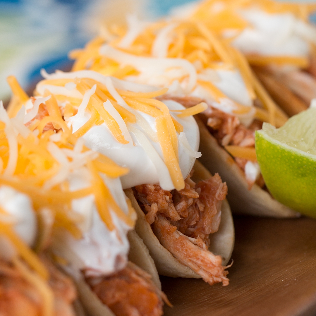 Close-up of shredded chicken tacos topped with cheese, sour cream, and lime wedges