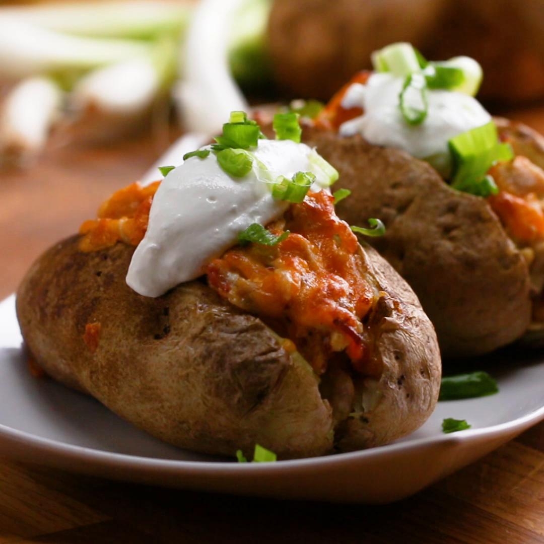 Baked potatoes topped with melted cheese, sour cream, and chopped green onions on a plate
