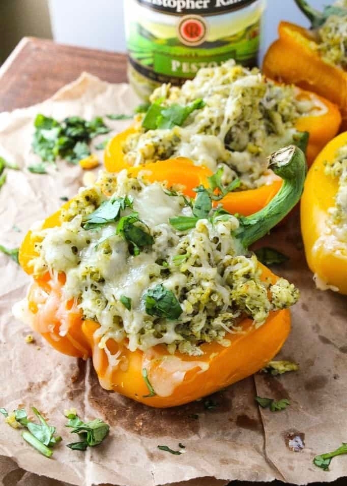 Stuffed bell peppers with a mix of rice, cheese, and herbs, served on parchment paper. A jar of pesto is visible in the background