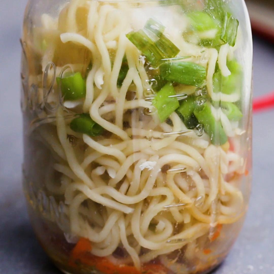 A jar filled with noodles, chopped green onions, and vegetables, showcasing a homemade instant noodle meal