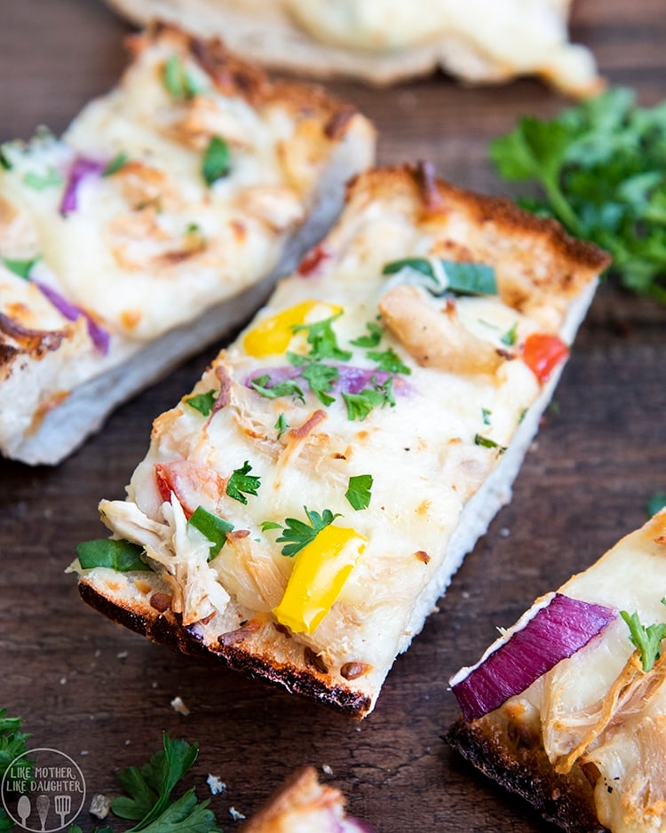 Slices of chicken and vegetable-topped cheesy bread garnished with herbs on a wooden surface