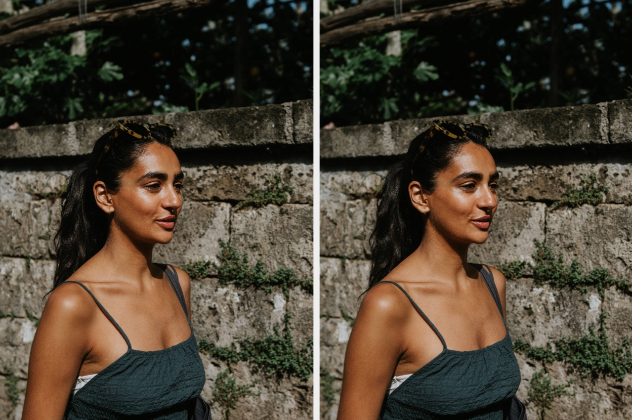 Woman outdoors with long hair in a ponytail, wearing a sleeveless dress. She is standing by a stone wall, smiling and looking into the distance