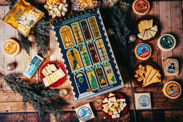 Assorted cheeses and a cheese-themed advent calendar are artfully arranged on a wooden table with festive decorations