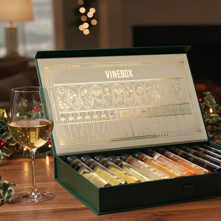 Open wine box with 12 tubes of different wines next to a filled wine glass on a festive table