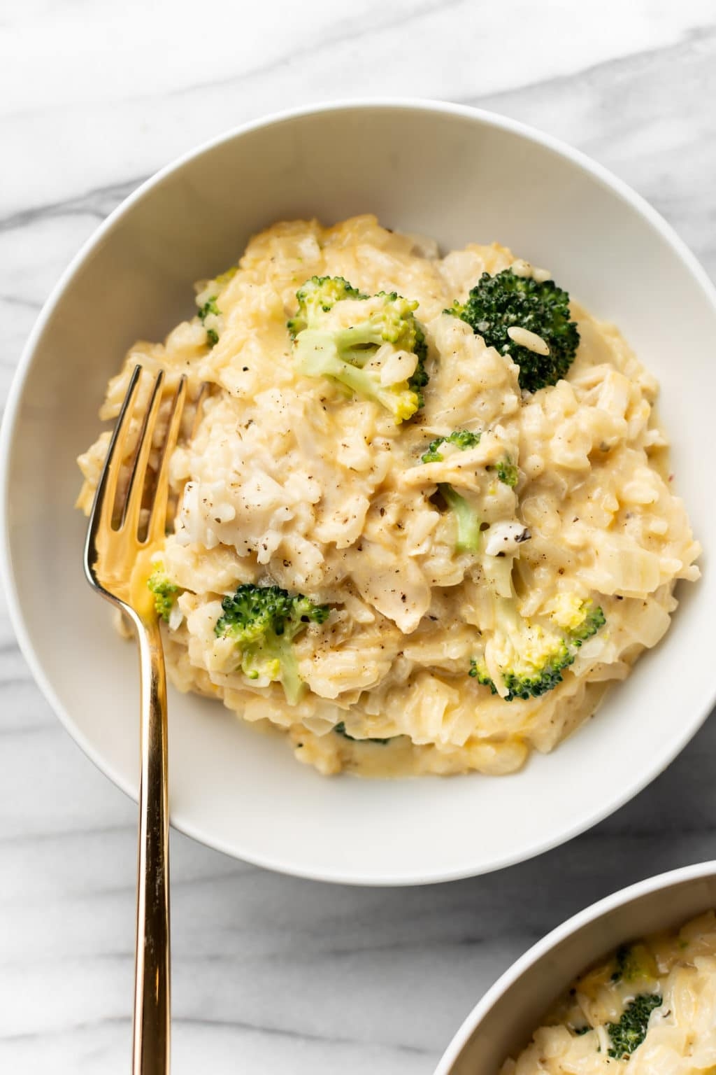 Creamy risotto with broccoli and cheese in a white bowl, accompanied by a gold fork