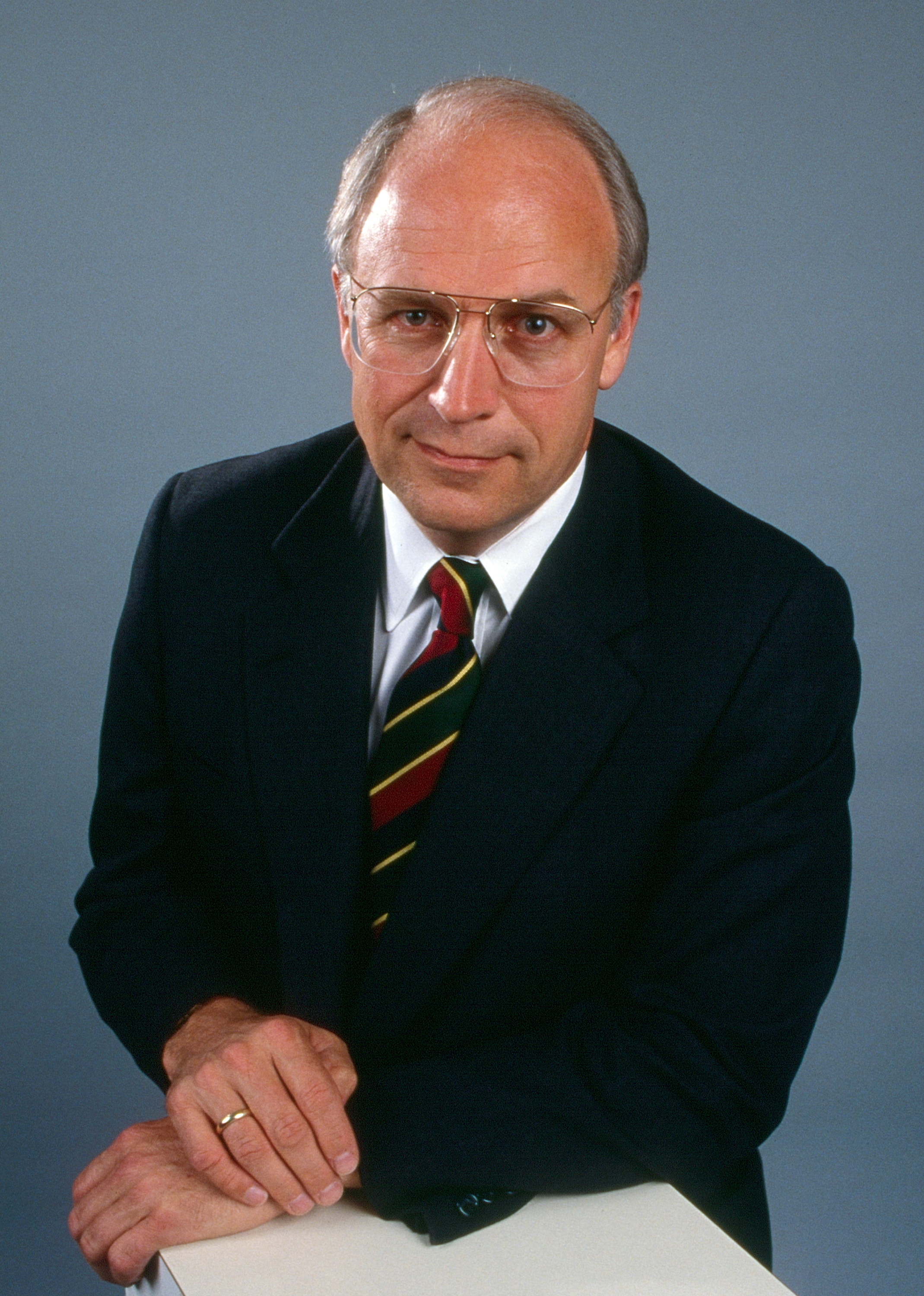 Person iført dress og stripet slips, lener seg på en overflate, ser på kameraet, med nøytral bakgrunn