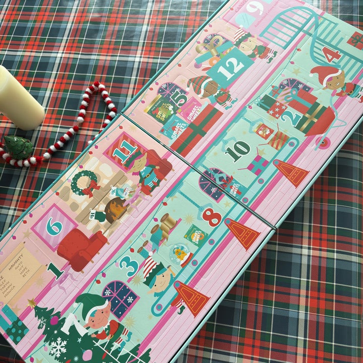 Advent calendar with numbered doors, festive illustrations of gifts, and holiday scenes on a plaid tablecloth