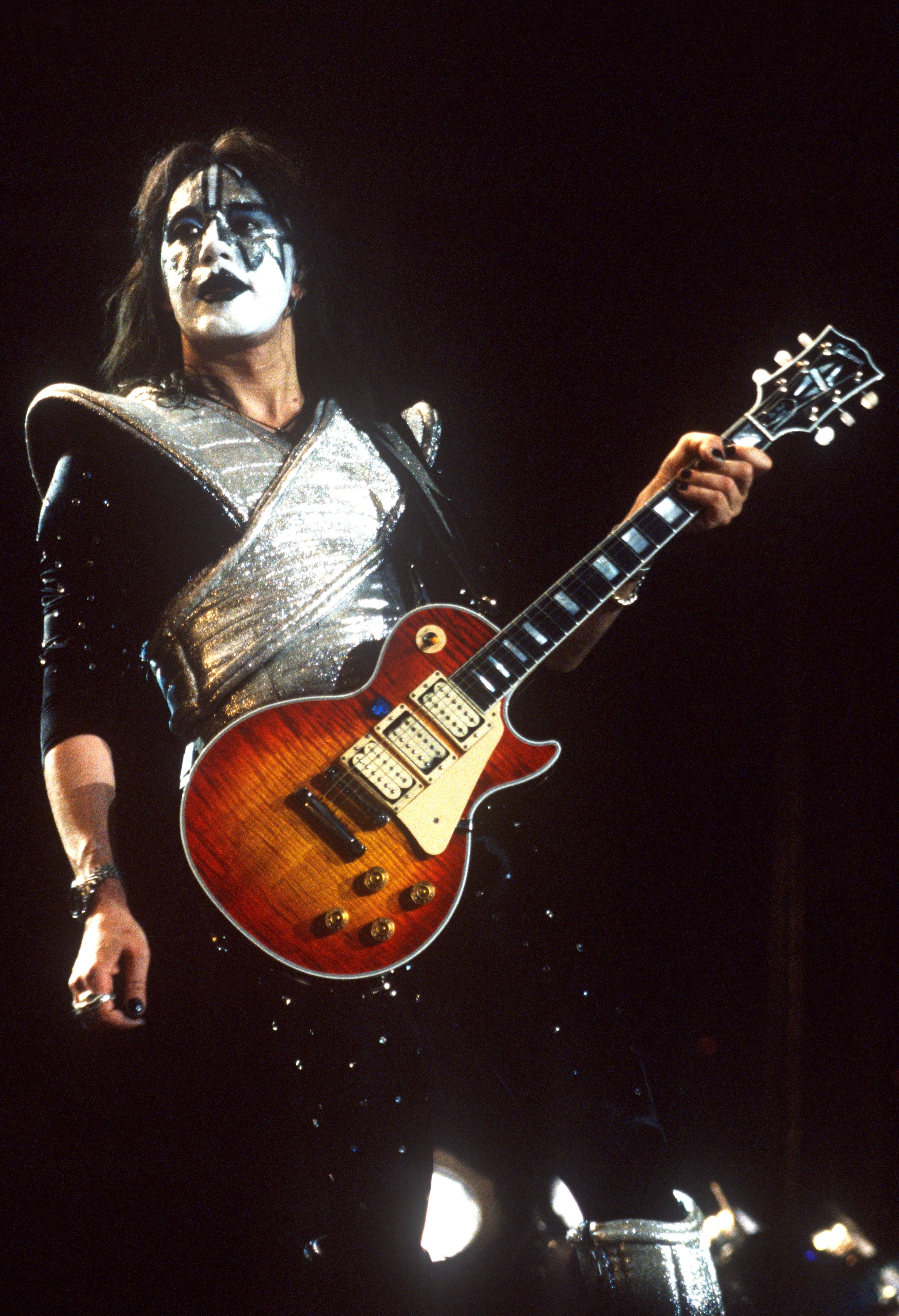 Musiker i kostyme med romtema og ansiktsmaling spiller elektrisk gitar på scenen