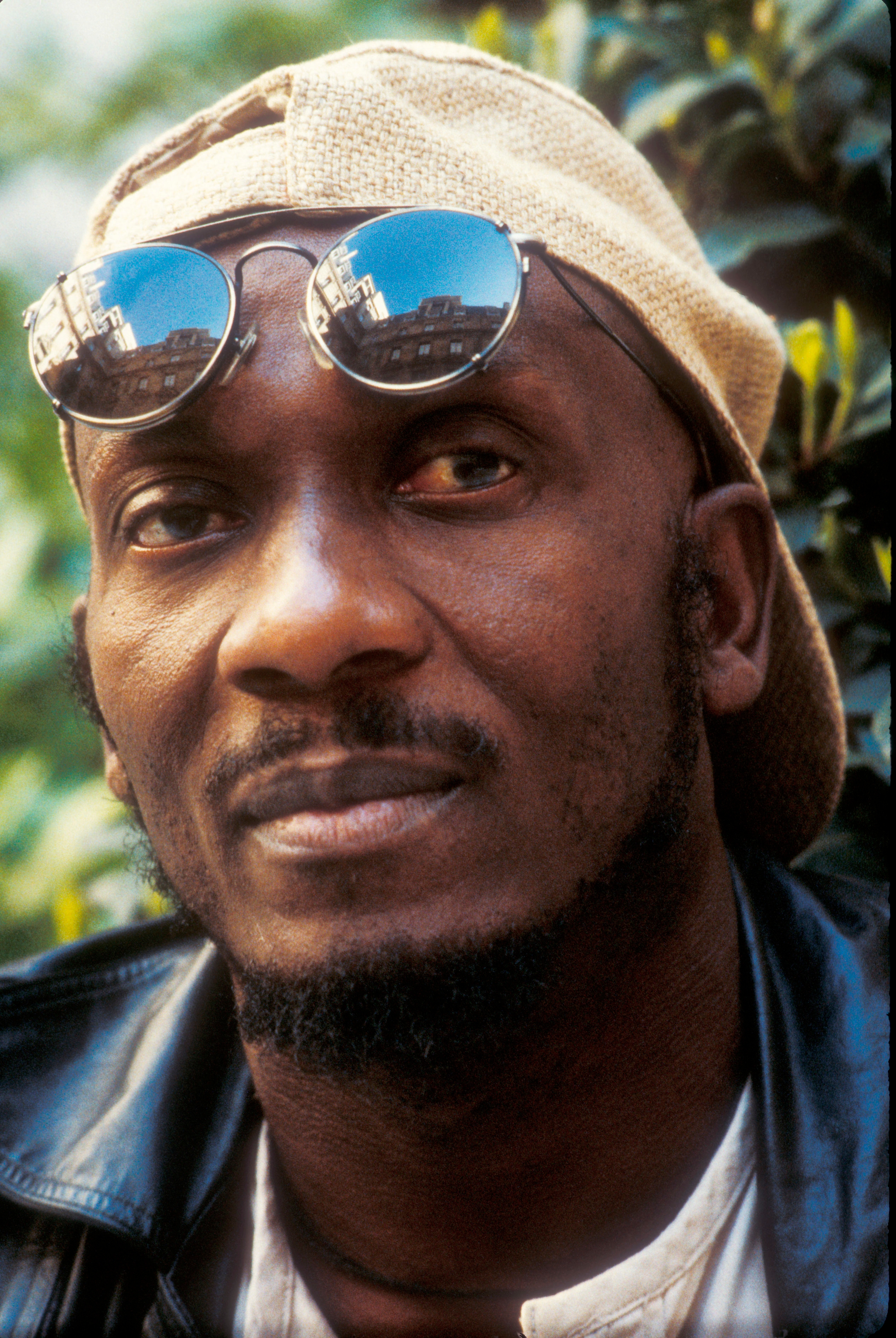 Mann iført en baklengs caps, runde solbriller på toppen, og en skinnjakke, utendørs