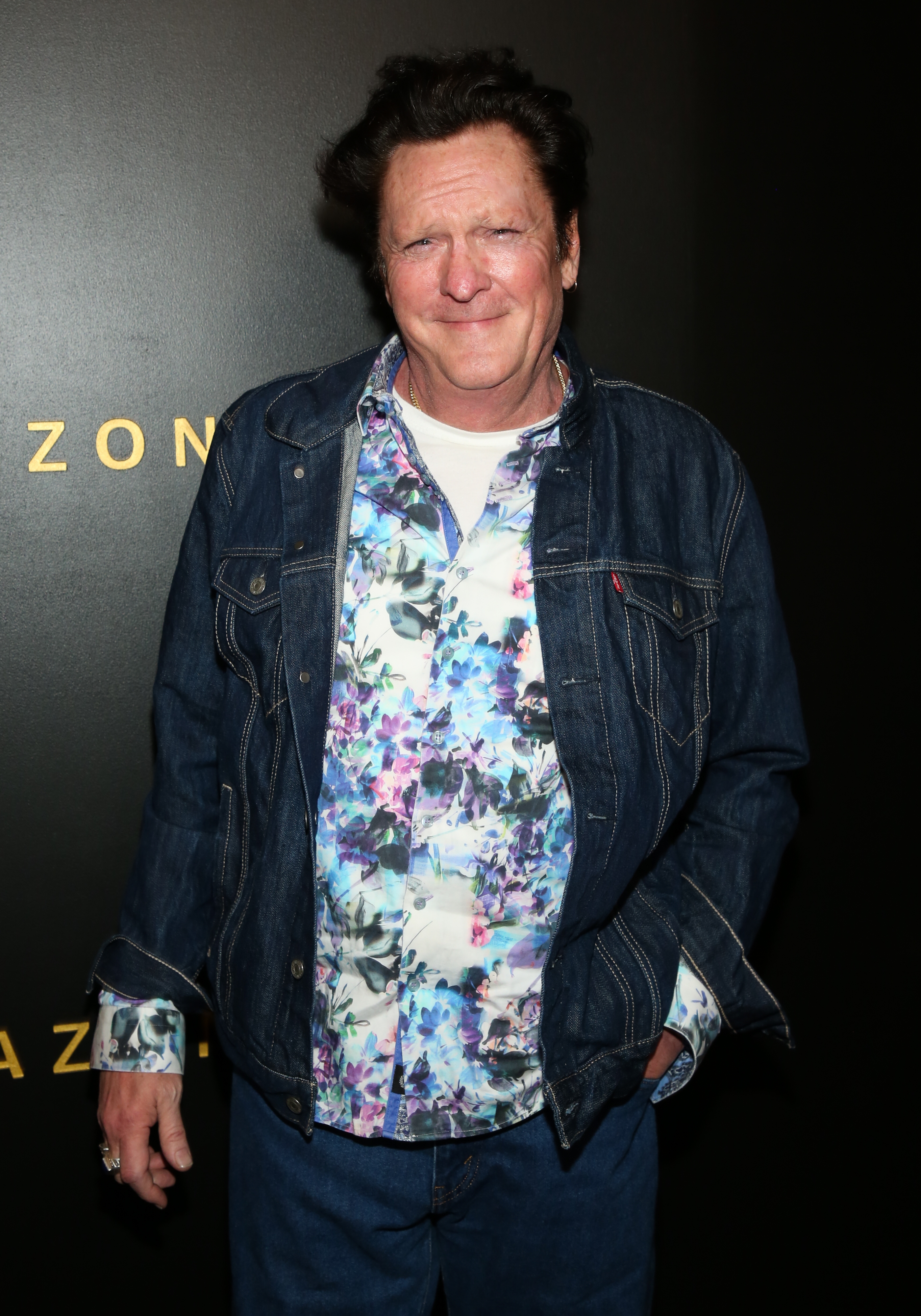 En person i en blomsterskjorte og dongerijakke poserer på en mediebegivenhet